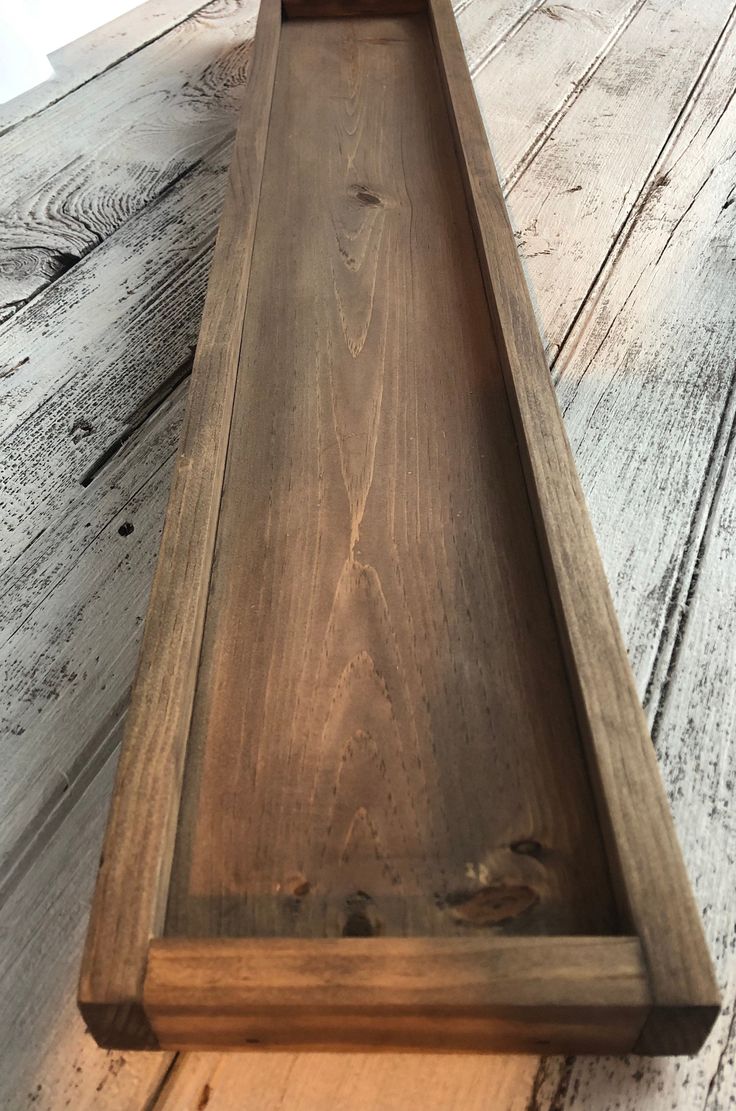 an empty wooden tray sitting on top of a white wood floor next to a wall