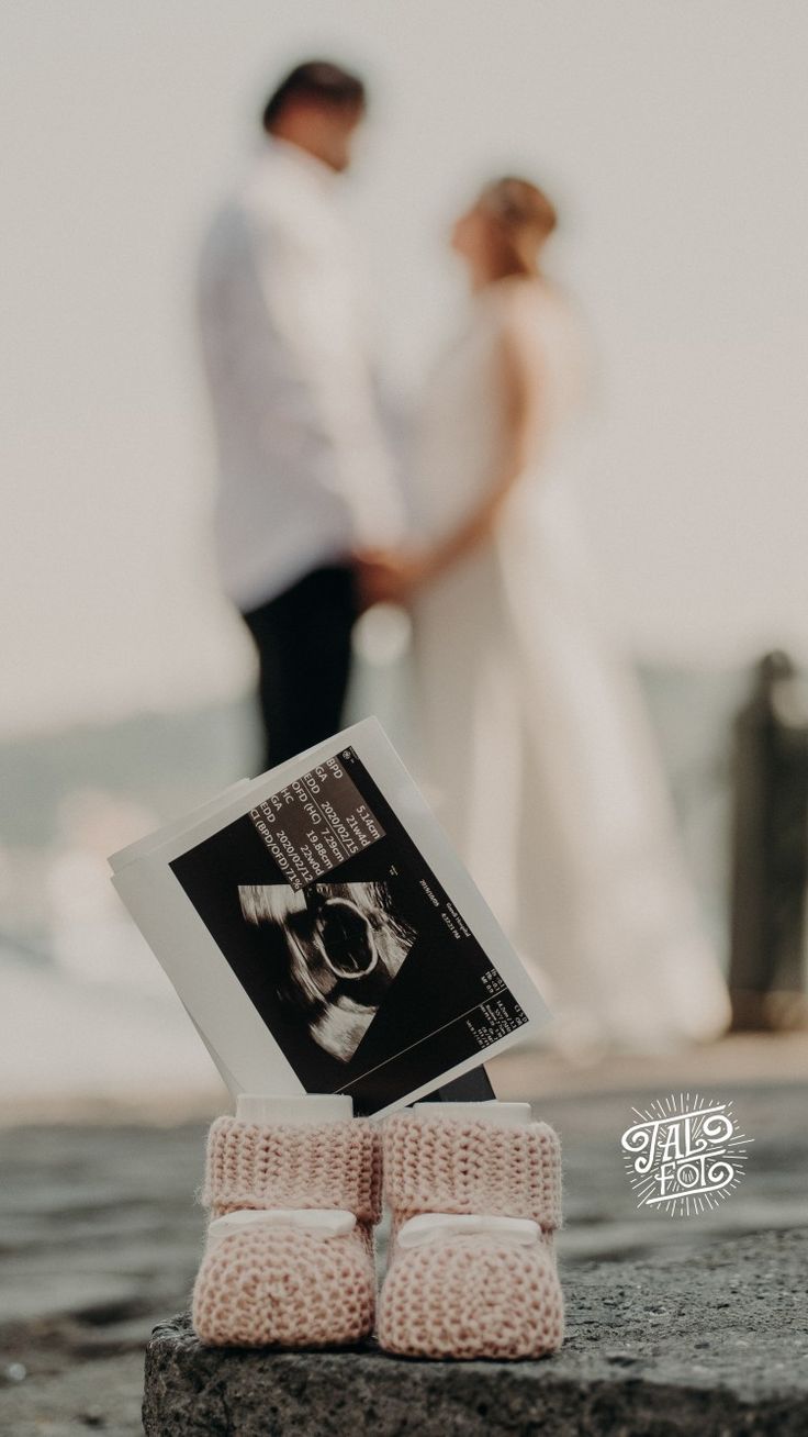 a couple standing next to each other on top of a stone slab near the ocean