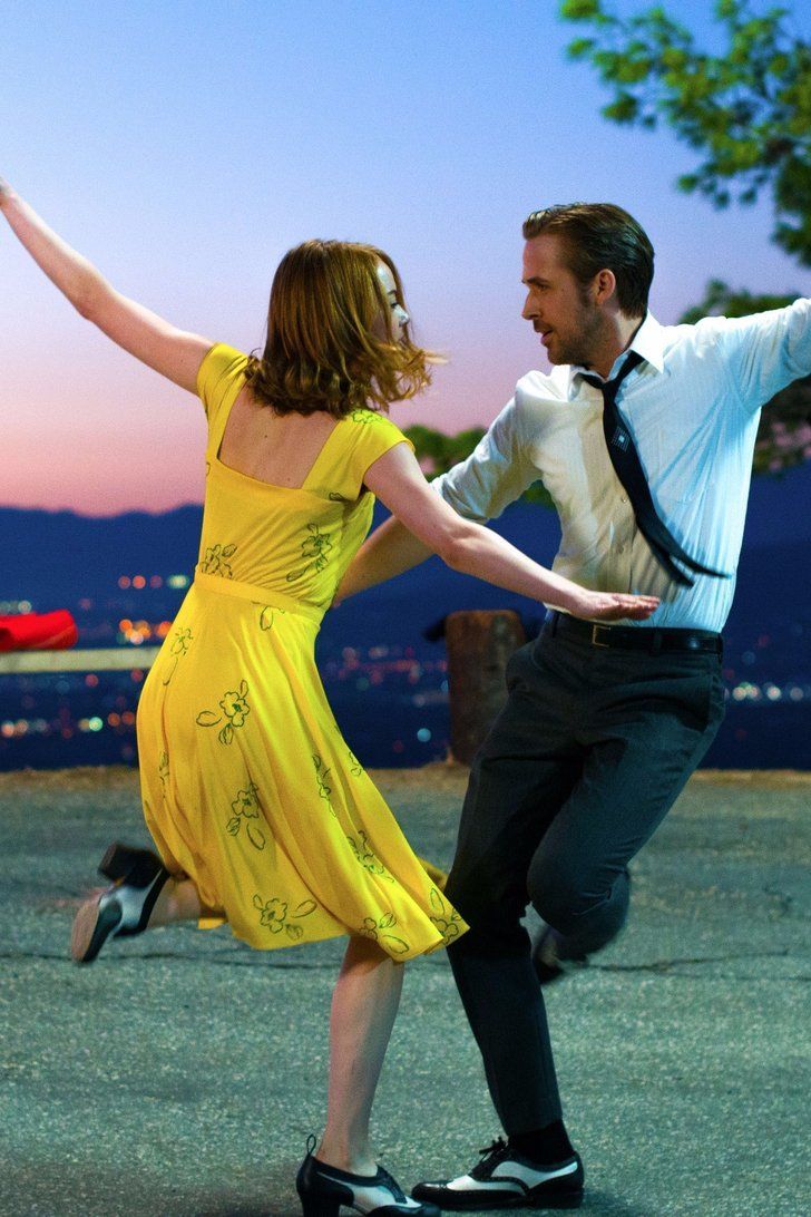 a man and woman are dancing together in the park at night with city lights behind them