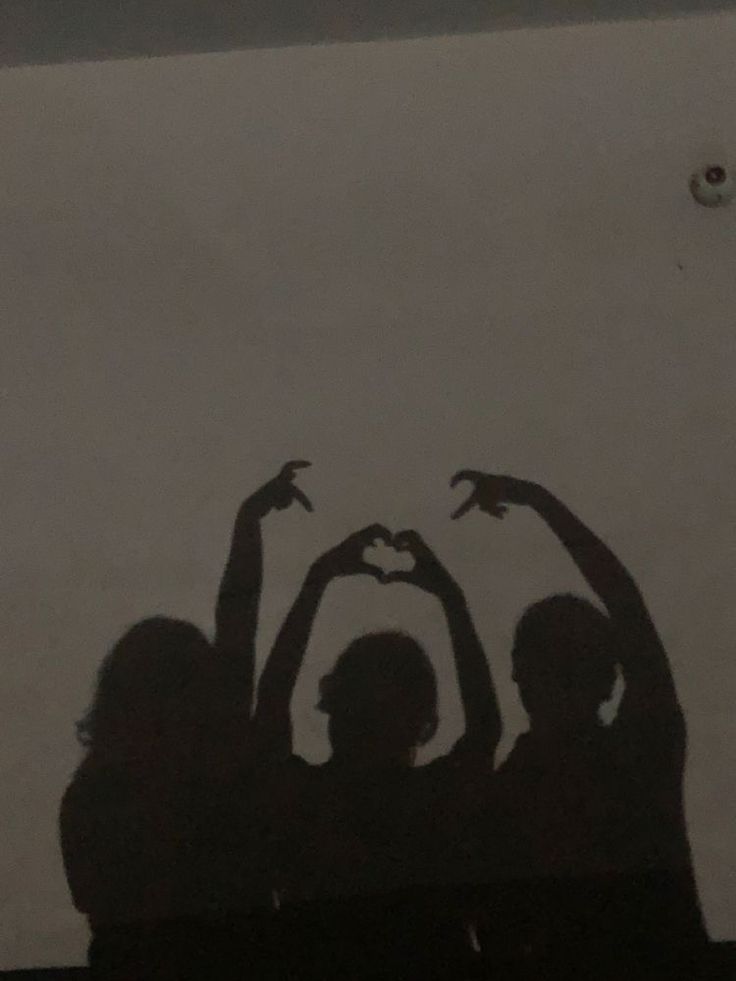 three people holding their hands up in the shape of a heart with one person's shadow