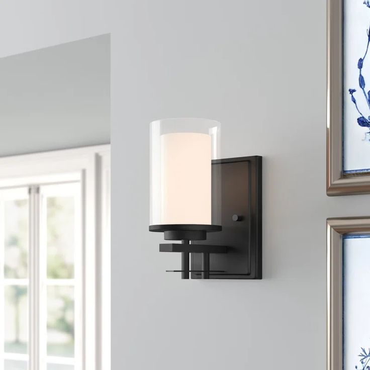 a wall light mounted on the side of a white wall next to two framed pictures