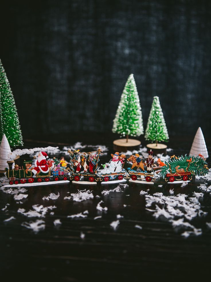 a table topped with small christmas trees and miniature train cars on top of snow covered ground