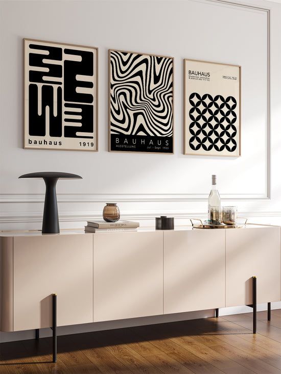 three black and white art pieces hang on the wall above a buffet table in an empty room