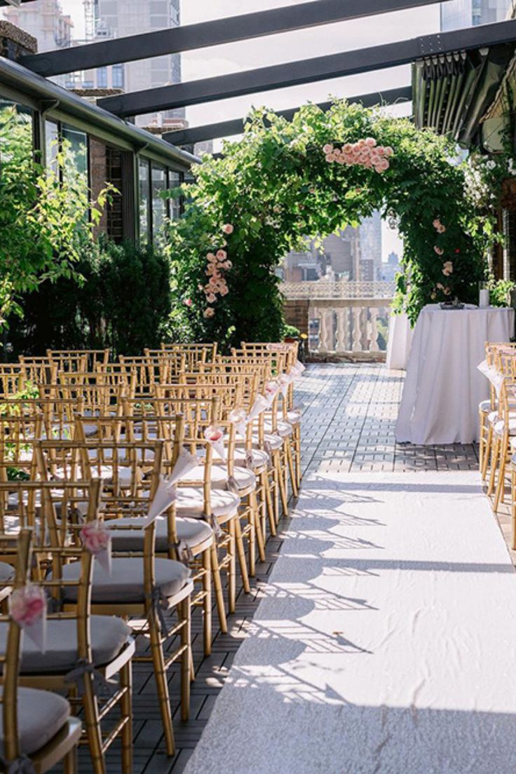 an outdoor ceremony setup with gold chairs and white tablecloths, surrounded by greenery