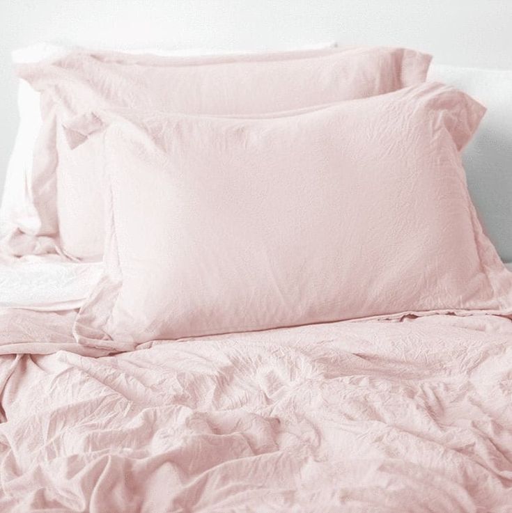 a bed with pink sheets and pillows on top of it in front of a white wall