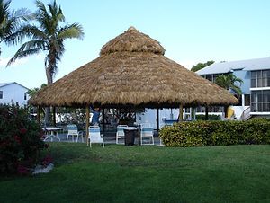 a thatched umbrella sitting on top of a lush green field next to palm trees