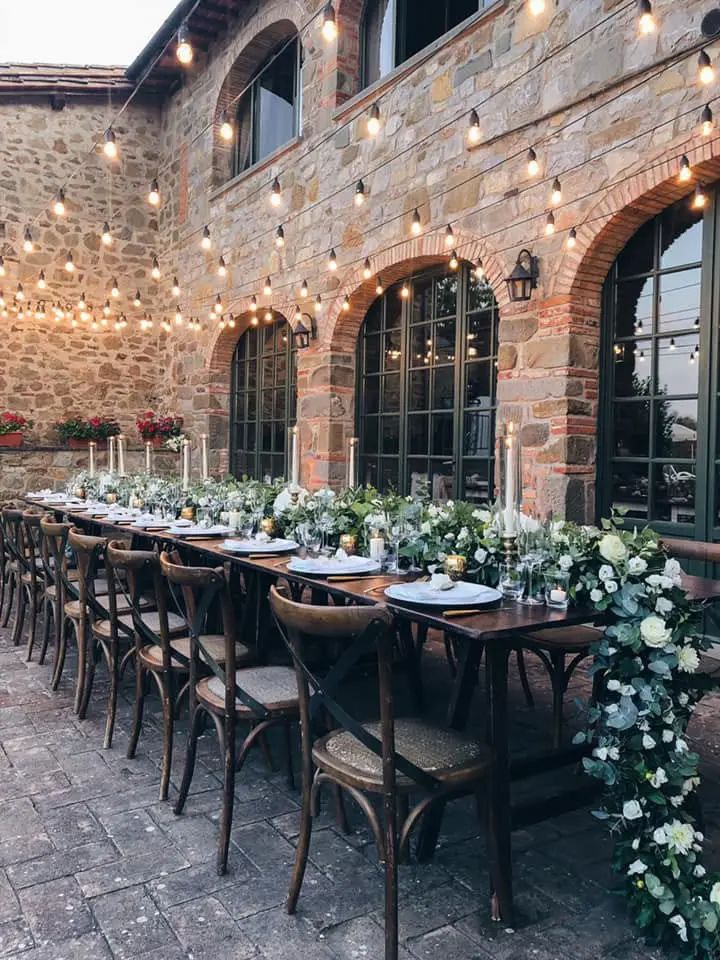 a long table set up with flowers and candles for an outdoor wedding reception at the stone building