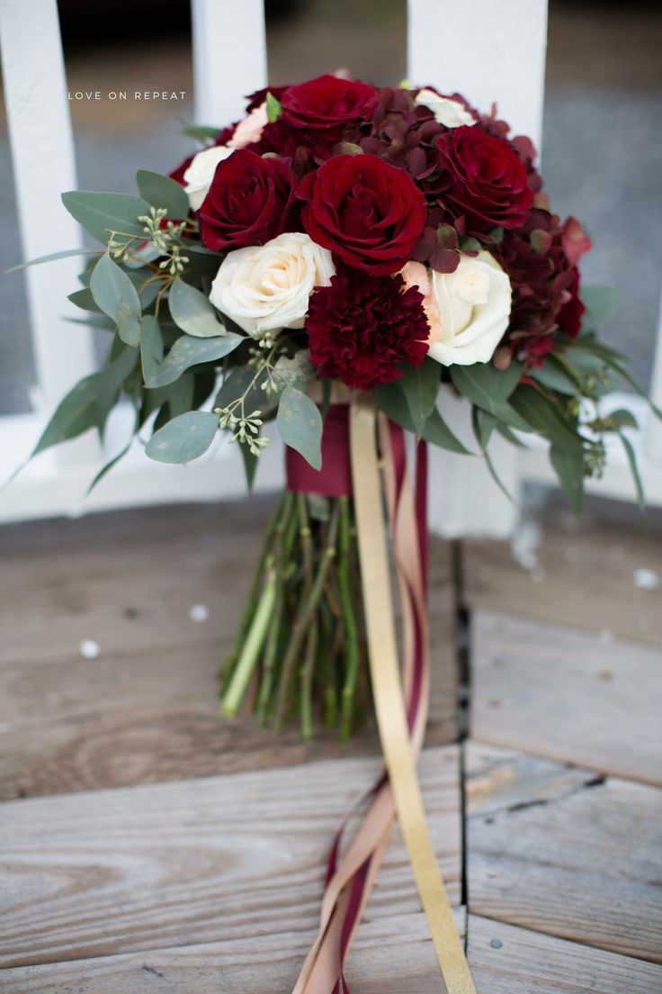 a bouquet of red and white flowers sitting on top of a wooden table next to a chair