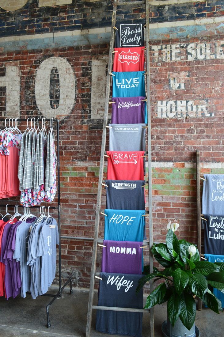 an old ladder is used to store t - shirts in front of a brick wall