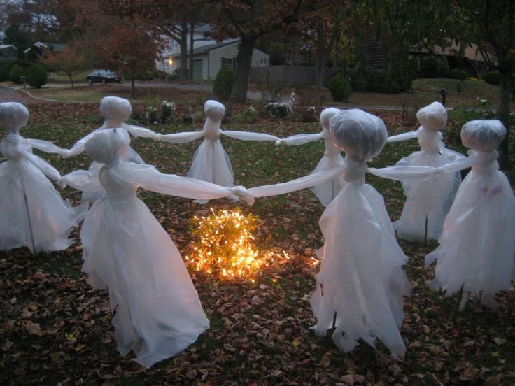 several white plastic figures are holding hands over a fire pit in the middle of leaves