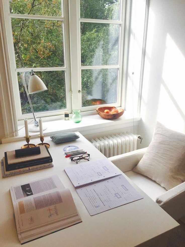 a desk with some books on it and a lamp next to the window sill