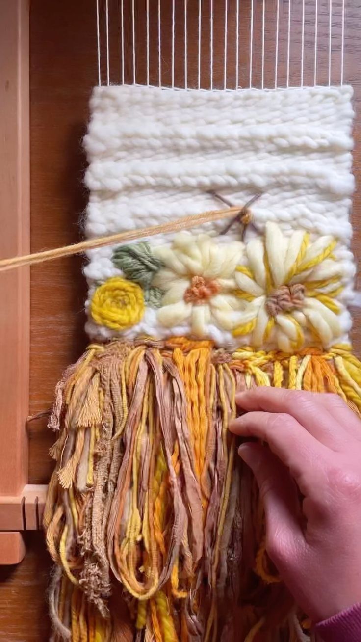 someone is weaving something on a loom with yarn and flowers in the center,