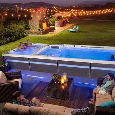 an outdoor hot tub is lit up at night with people lounging in the background