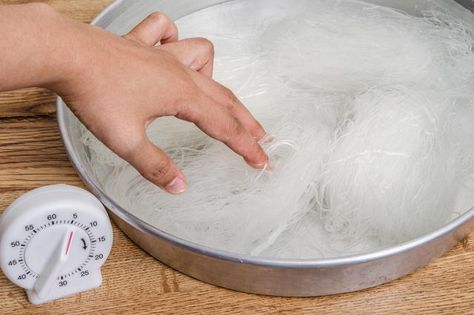 a person's hand reaching for something that is boiling in a pan on a wooden table