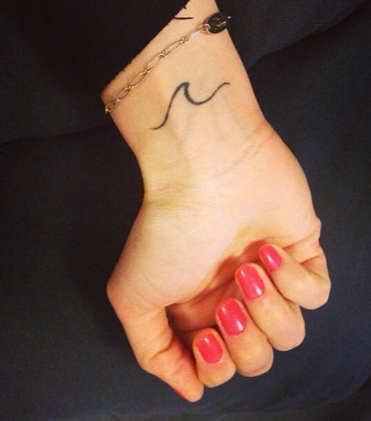 a woman's hand with a small wave tattoo on her left wrist and red nail polish