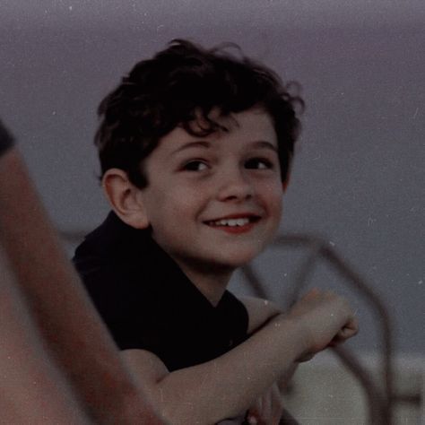 a young boy is smiling and holding his arm around someone's shoulder while sitting on a bed