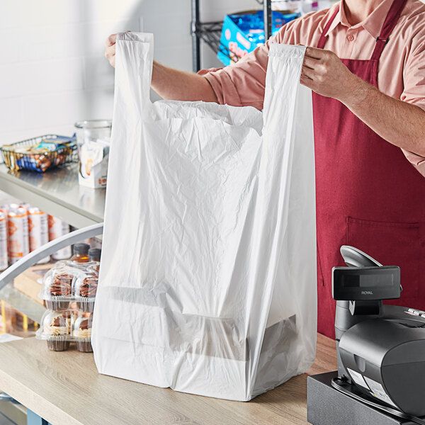 a man in an apron is holding a white bag while standing at a cash register