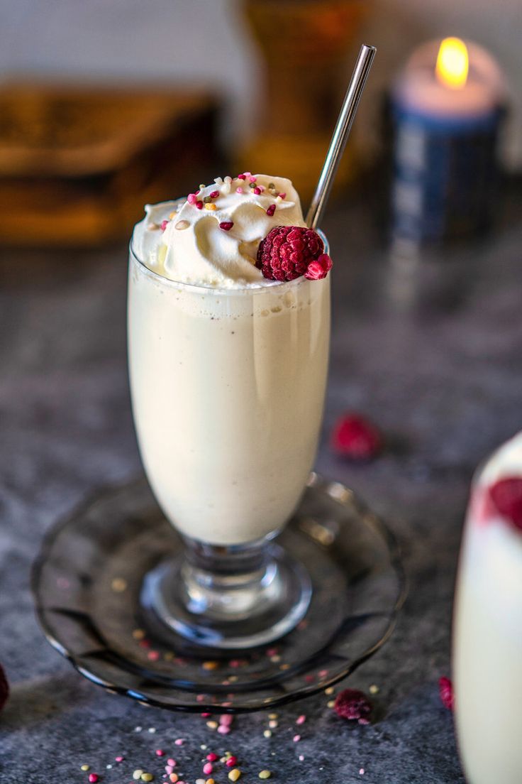 a dessert with whipped cream and raspberries in a glass on a table next to a candle