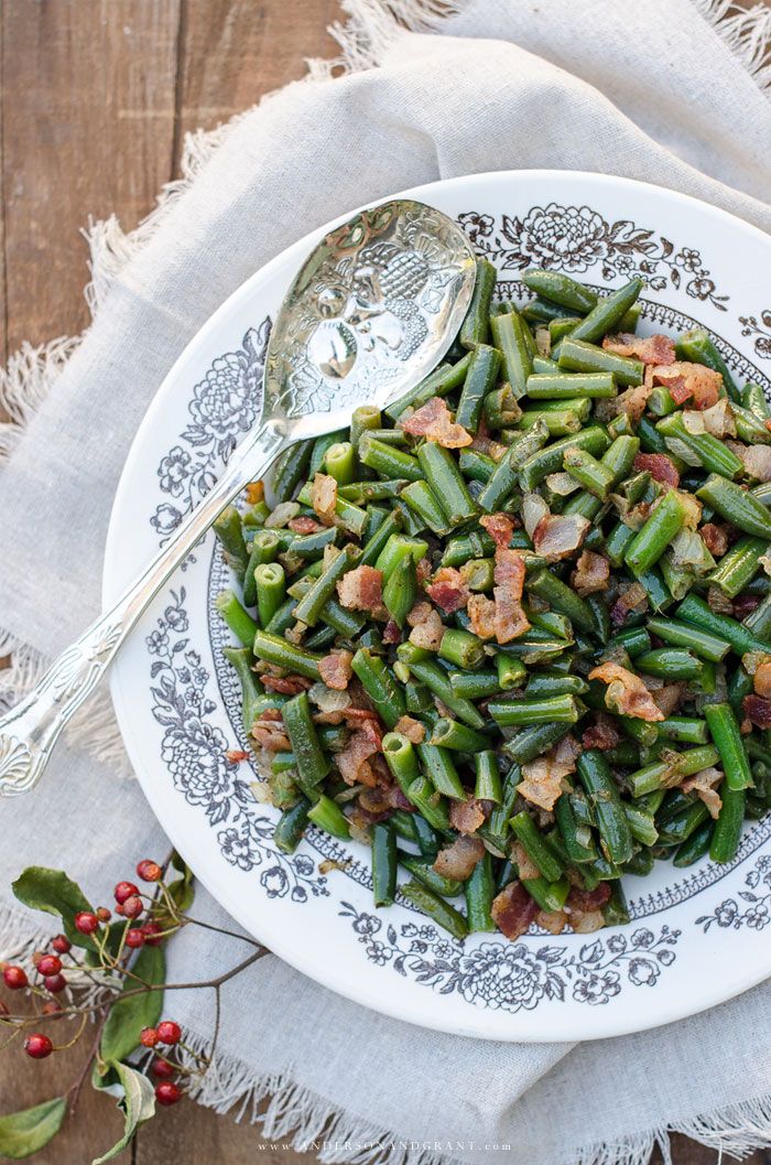 a white plate topped with green beans and bacon next to a silver spoon on top of a table