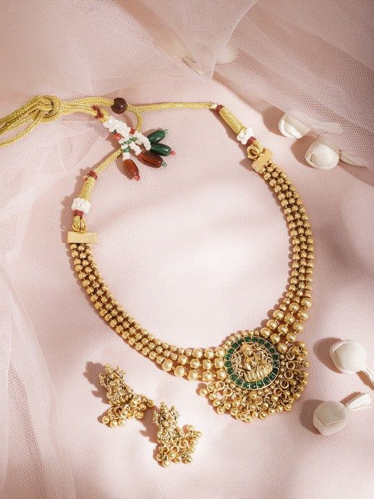 This jewellery set consists of a necklace and a pair of earringsThe gold-plated necklace has a green/red stone-studded Lakshmi motif, secured with a draw-string closureA pair of matching drop earrings, each secured with a post and back closure. Size & Fit Necklace: 21 cmEarrings: 2.5 cm Material & Care Material: BrassPlating: Gold-platedStone Type: Artificial stones Care Instruction Wipe your jewellery with a soft cloth after every useAlways store your jewellery in a flat box to avoid accidental scratchesKeep sprays and perfumes away from your jewelleryDo not soak your jewellery in waterClean your jewellery using a soft brush, dipped in jewellery cleaning solution only Dispatch within 7 days Gold Plated Meenakari Jewelry For Puja, Temple Jewelry Sets With Latkans And Round Shape, 22k Gold Jewelry For Navratri, Gold Plated Temple Jewelry Sets, Gold Plated Chandbali Jewelry For Navratri, Round Kundan Necklace With Latkans In Temple Style, Temple Jewelry Style Kundan Necklace With Latkans, Yellow Gold Kundan Necklace For Navratri Gift, Round Temple Necklace With Latkans For Diwali