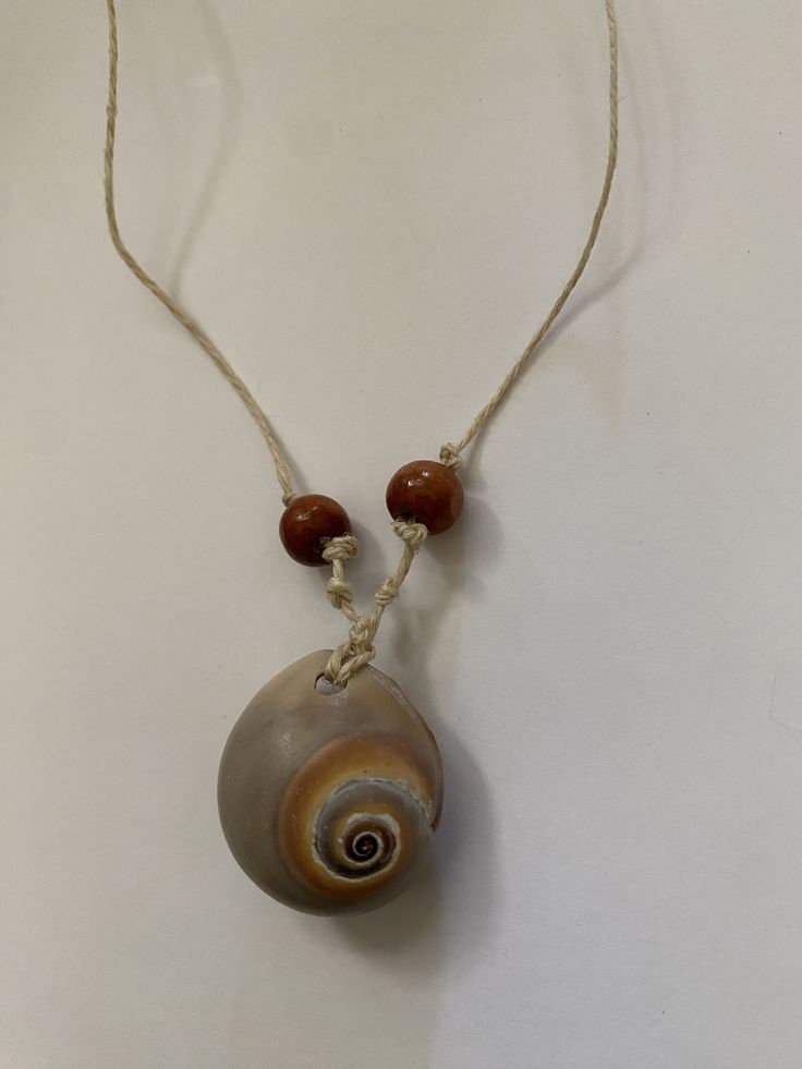 a necklace with a shell and two beads hanging from it's side on a white surface