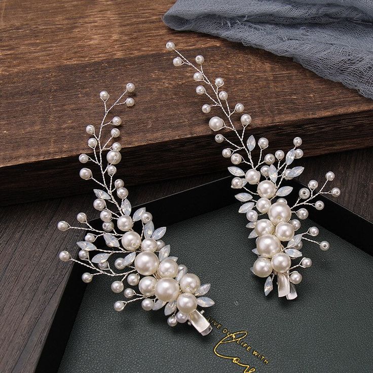 two wedding hair combs with pearls and leaves on top of a black box next to a wooden table