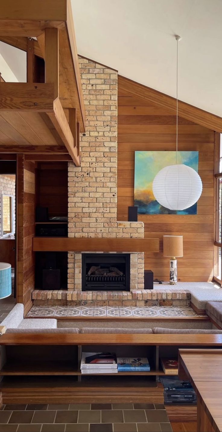 a living room with a large brick fireplace in the center and wood paneling on the walls