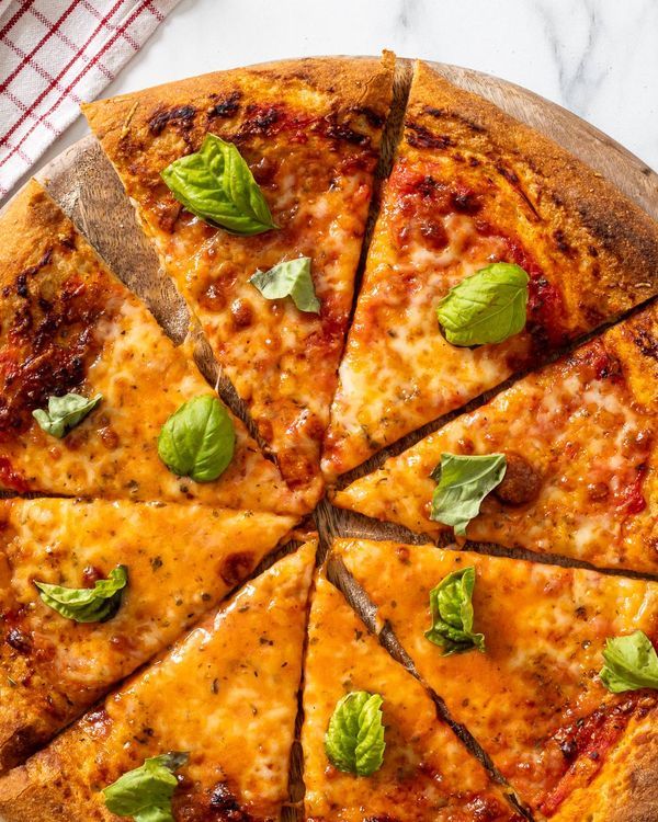 a pizza that is cut into eight slices on a wooden platter with basil leaves