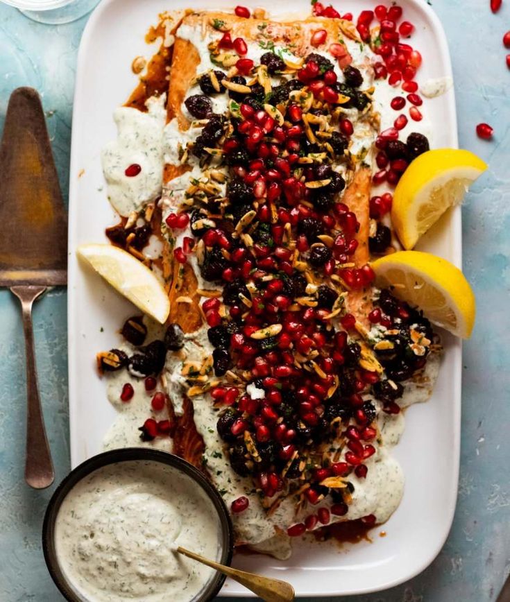 a white plate topped with fish covered in pomegranates and lemon wedges