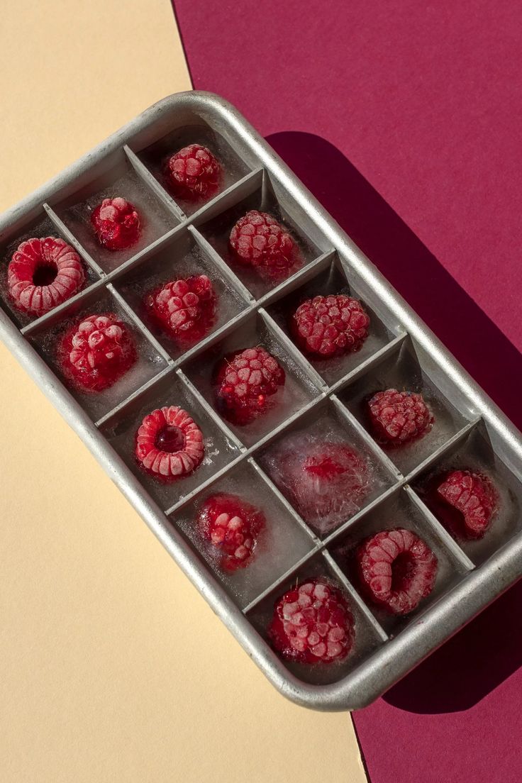 raspberries in an ice cube tray on a pink and yellow tablecloth with shadows