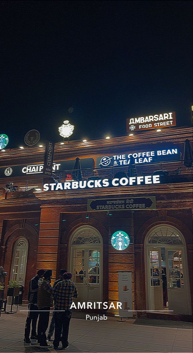 three people standing in front of a starbucks coffee shop at night with the lights on