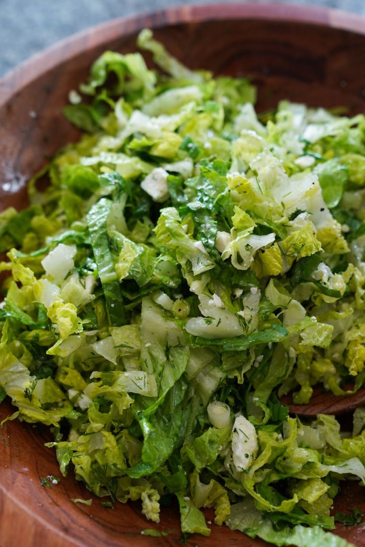 a wooden bowl filled with lettuce on top of a table