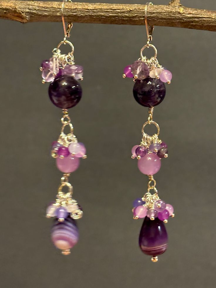 Artisan designed and handmade, dangling Pink and Purple Amethyst, Red Purple Jade, Pink and Lavender Jade Gemstones Chandelier Cluster Earrings. Exceptional colors purple, lavender and pink. From the top deep rich purple, 12 mm amethyst round bead underneath a cluster of pink, purple, and lavender.  These earrings are splendid dazzling beads, lavender jade 8 mm round, dangling beneath the second cluster. The final bead is chalcedony banded agate and underneath the third cluster gemstones.  These Cluster Chandelier, Lavender Jade, Pink And Lavender, Beaded Earrings Diy, Purple Jade, Earrings Diy, Rich Purple, Colors Purple, Pink Jewelry