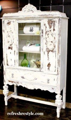 an old white cabinet with glass doors and drawers on the bottom shelf is displayed in front of a black wall