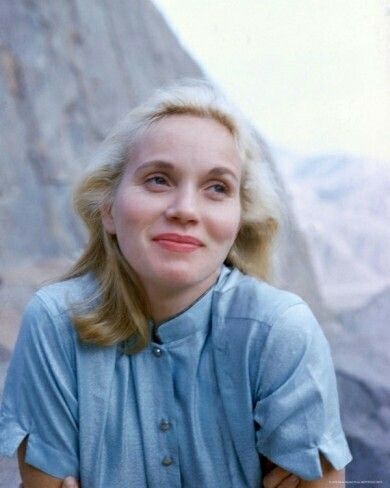 a woman standing in front of a mountain with her arms crossed and looking at the camera