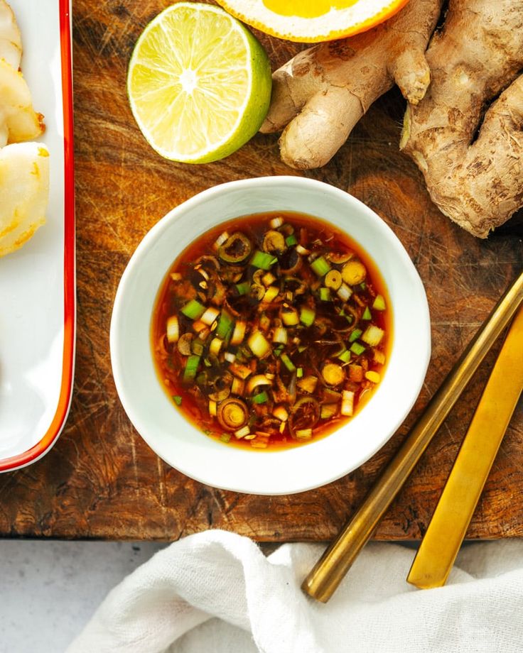 a wooden cutting board topped with a bowl of soup next to sliced lemons and ginger