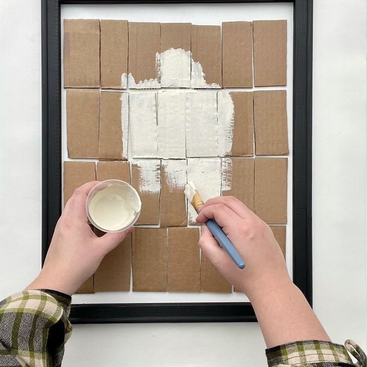 a person is holding a paintbrush and painting squares on the wall with white paint