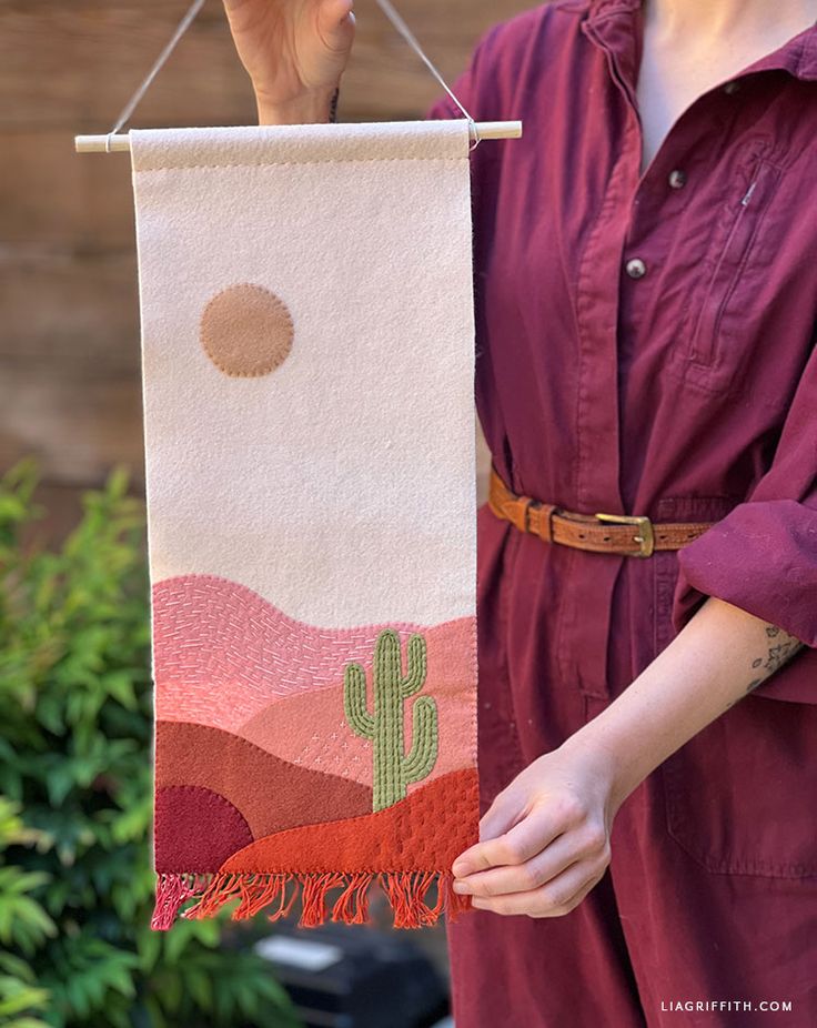 a woman is holding up a towel with a desert scene on it and a cactus in the background