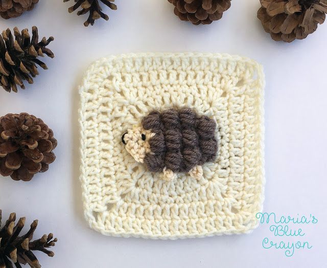 a crocheted square with a sheep on it surrounded by pine cones