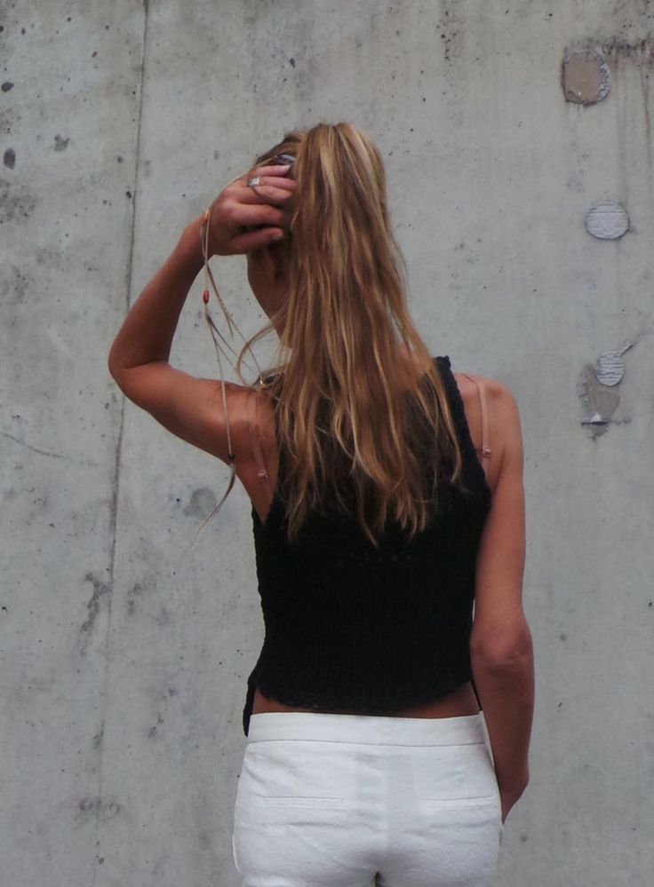 a woman standing in front of a wall with her hand on her head and wearing white pants