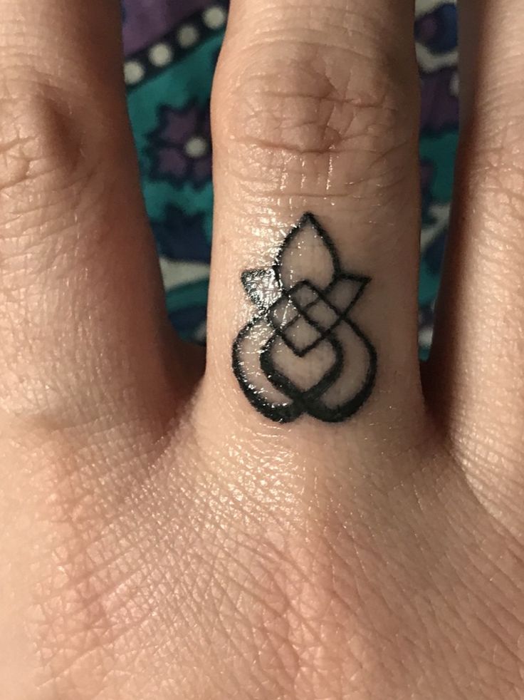 a person's hand with a small black and white tattoo on the middle finger