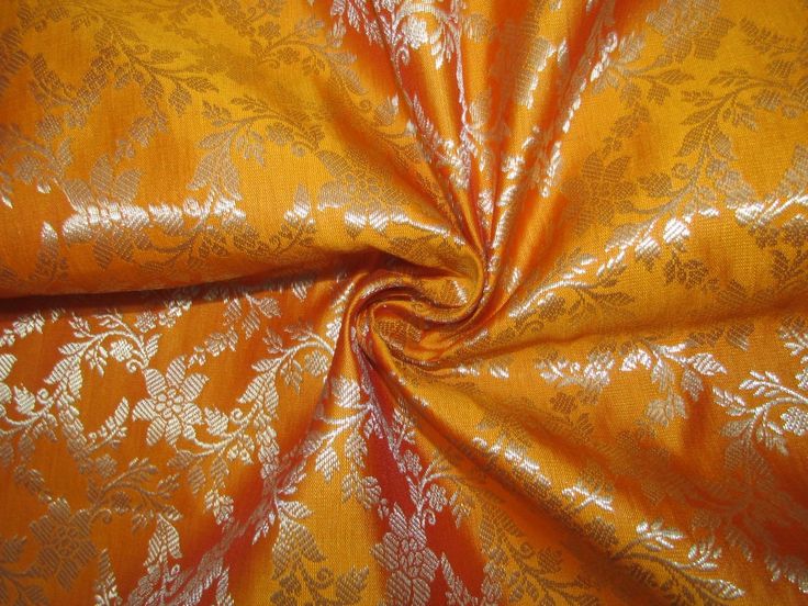 an orange and gold fabric with white flowers on the top, as well as leaves