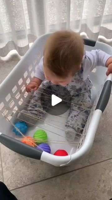 a baby sitting in a laundry basket playing with balls and yarns on the floor