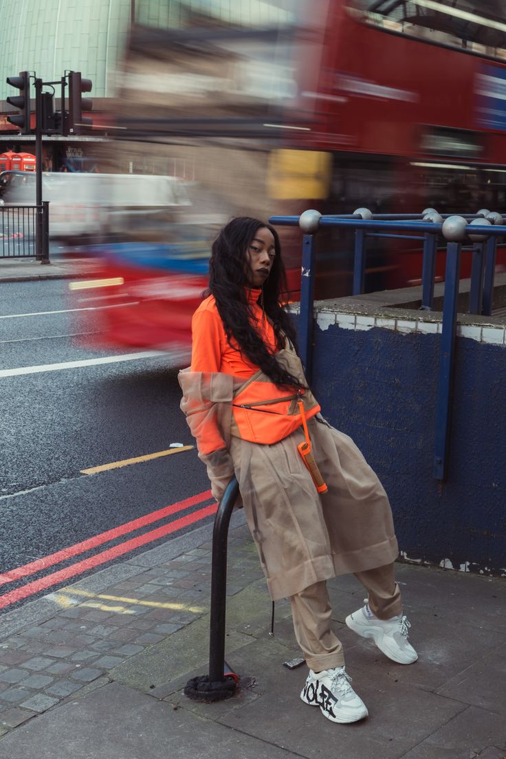 a woman standing on a street corner next to a pole with a bus in the background