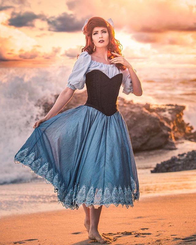 a woman in a blue dress is standing on the beach