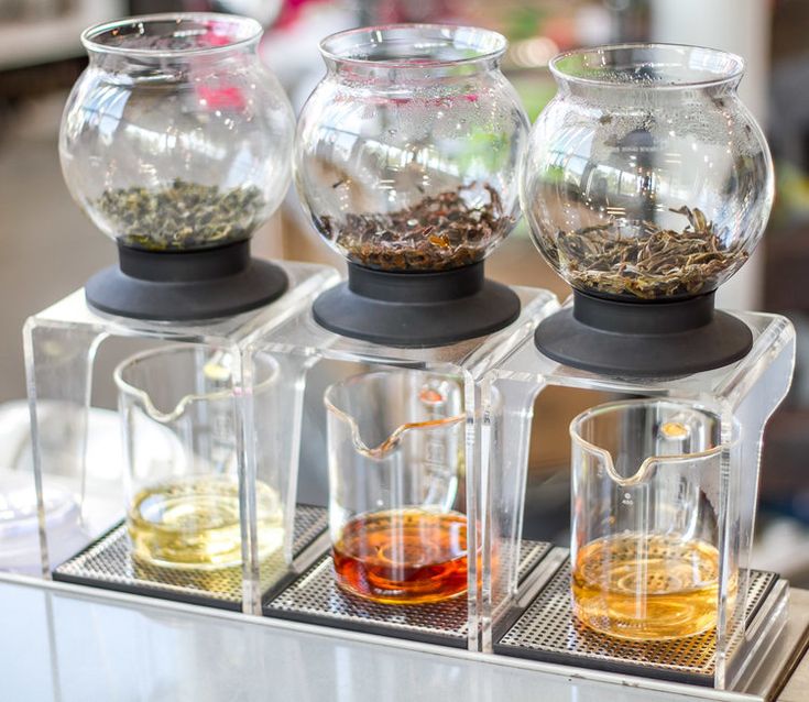 three glass containers filled with different types of tea on a metal tray next to each other