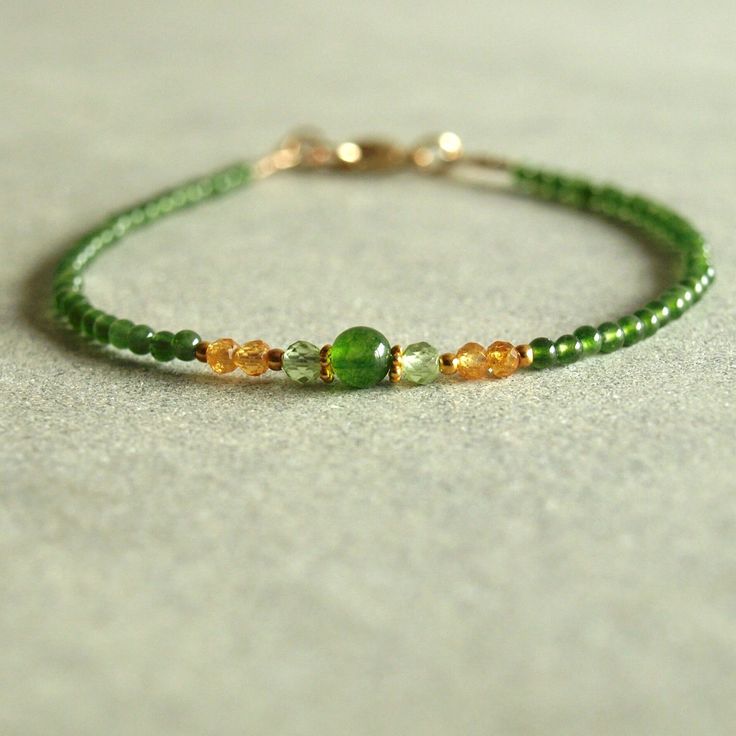 Small smooth green jade lead to Mandarin orange garnet, light green peridot, and 18K solid gold beads which frame a lovely smooth round green jade at the center of this solid gold bracelet. This minimal women's jewelry bracelet closes with a 14K solid gold lobster clasp and loop. The colors of these dainty gemstones are so striking together. The natural jade is round, green, and smooth, a lovely green jade color. The Mandarin orange garnet and light green peridot look beautiful beside the larger Green Dainty Beaded Bracelets With Natural Stones, Dainty Green Beaded Bracelets With Natural Stones, Dainty Green Gemstone Beaded Bracelets, Dainty Green Beaded Bracelet With Natural Stones, Elegant Peridot Round Beads Jewelry, Elegant Green Hand-strung Jewelry, Green Gemstone Rondelle Jewelry, Green Peridot Jewelry With Gemstone Beads, Green Rondelle Gemstone Jewelry