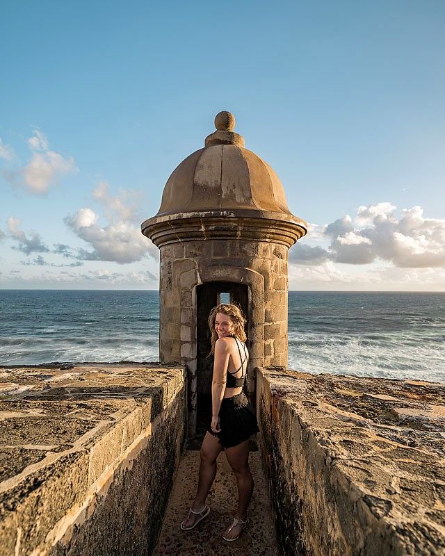 a woman standing at the entrance to an old structure by the ocean on a sunny day