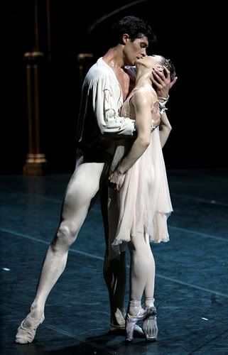 a man and woman in ballet clothes standing next to each other on a stage with their arms around each other