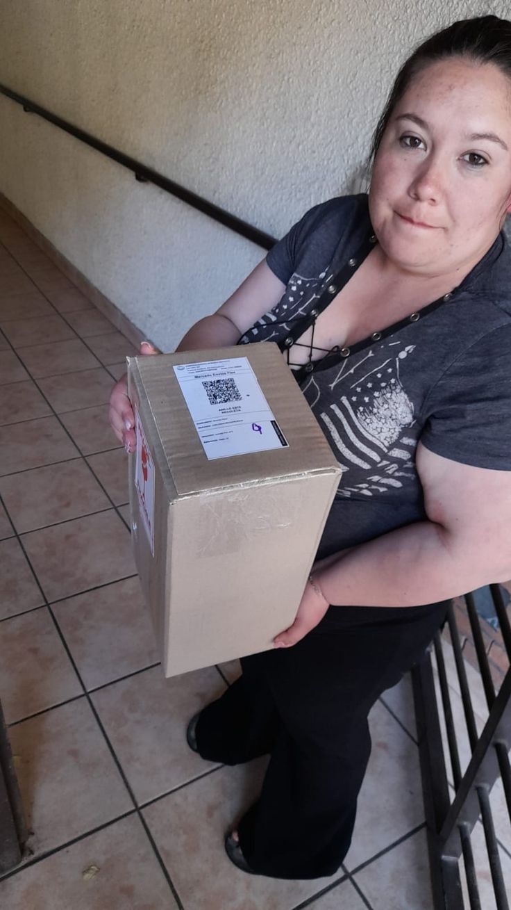 a woman is sitting on the stairs holding a box in front of her face and looking at the camera